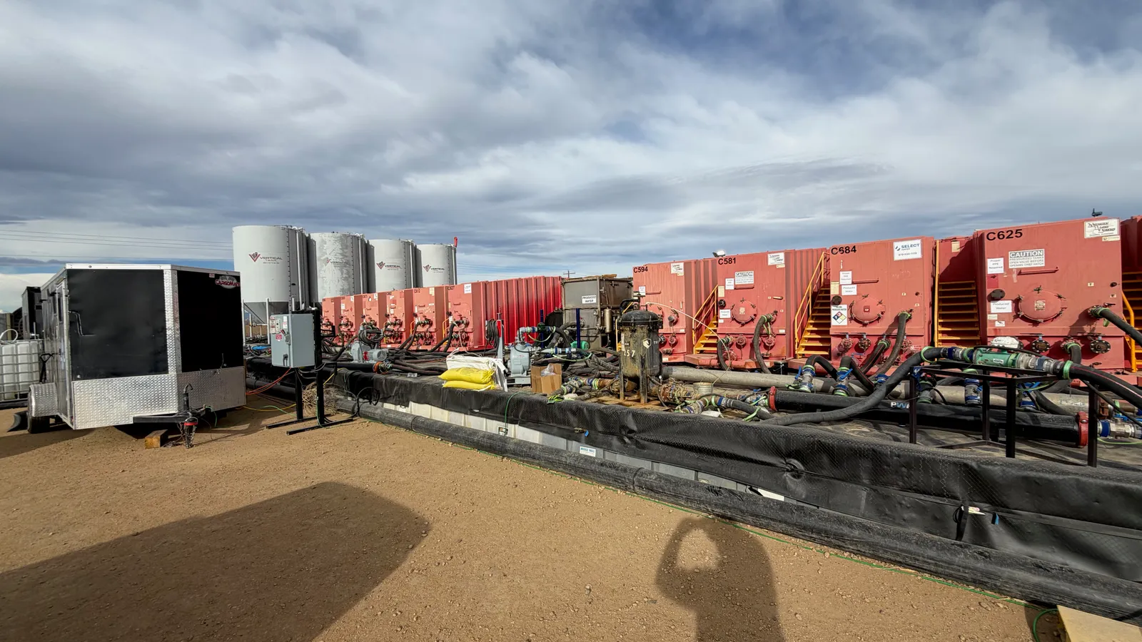 Frac tanks and vertical storage tanks lined up on a PWR location, manifolded together with lay-flat hose over lined containment.